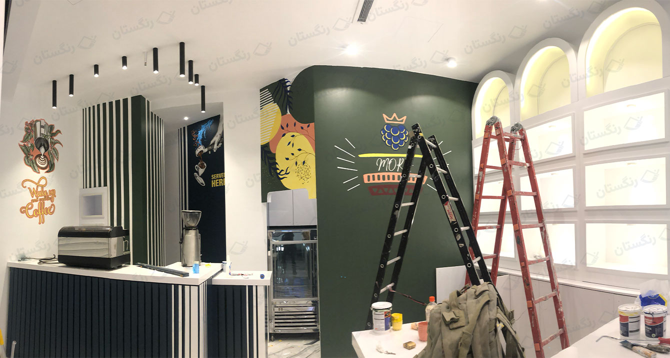 اجرای نقاشی دیواری کافه توسط تیم رنگستان؛ کار در مرحله تکمیل با نردبان، ابزار نقاشی و دیوار سبز طرح‌دار